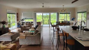 Un vaste espace de vie comprenant un canapé, une table à manger et des chaises, une cuisine dotée d’un grand îlot central et de grandes fenêtres offrant une vue sur l’extérieur.