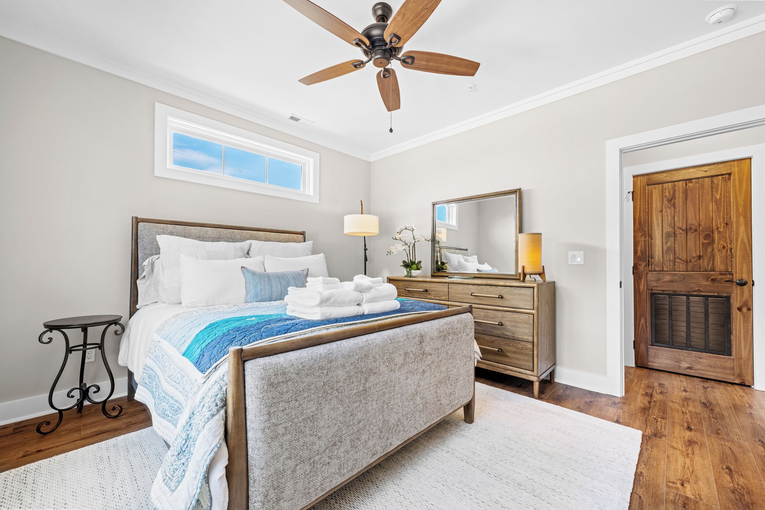 A bedroom with a bed, a wooden dresser, a ceiling fan, a window, and a door.