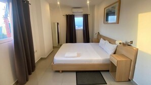 Una camera d'albergo con un letto grande, un comodino, tende a una finestra e un quadro appeso al muro.