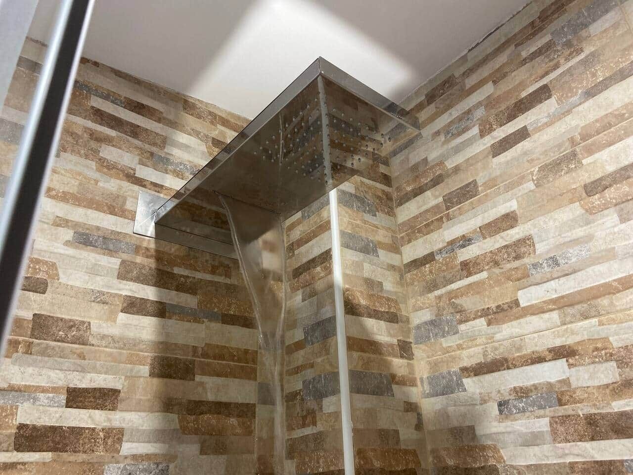 A shower with a glass enclosure and a stone-patterned wall.