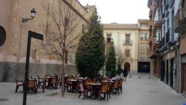 A narrow street with outdoor seating, a Christmas tree, and buildings on both sides.