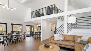 Ein großzügiger Wohnbereich mit hohen Decken, ein Essbereich mit großem Fenster und eine Treppe, die in einen oberen Bereich führt.