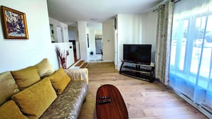 Ein Wohnzimmer mit einer Couch, einem Fernseher und einem Couchtisch. Eine Treppe führt in einen anderen Raum.