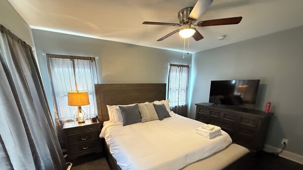 Une chambre d’hôtel avec un grand lit, un ventilateur de plafond, une télévision et une commode.