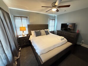 Habitación de hotel con una cama grande, ventilador de techo, televisión y cómoda.