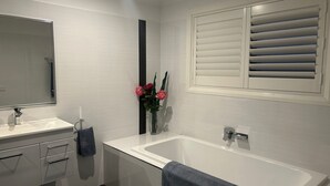 A modern bathroom with a white sink, mirror, and bathtub. There is a window with blinds, a towel rack, and a vase with flowers. - Lap of Luxury- Bathurst House
Very generous floor plan with dual living areas (Kelso)
