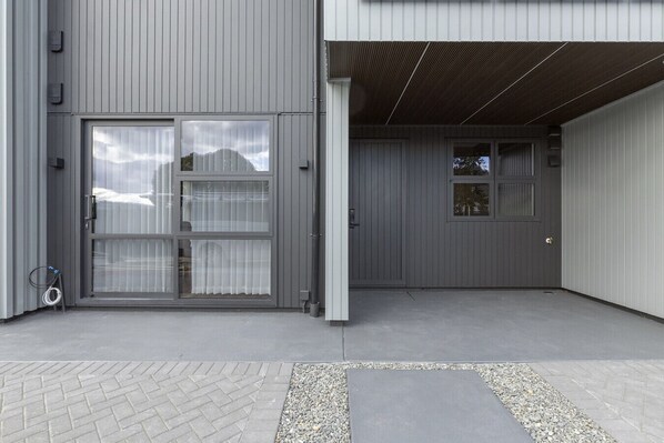 A modern building with a grey exterior, a large glass door with curtains, and a covered entrance area.