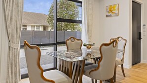 A dining area with a glass table and four chairs, a vase on the table, and a painting on the wall.