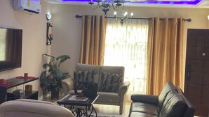 A living room with a sofa, a coffee table, a TV, and a chandelier. - 3-bedroom house at East Legon with 24hr security and solar powered lights (Accra)