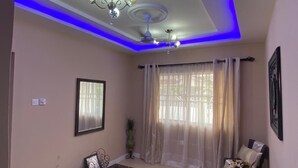 A living room with a ceiling fan, a chandelier, a sofa, a coffee table, and a window with sheer curtains. - 3-bedroom house at East Legon with 24hr security and solar powered lights (Accra)