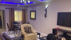 A living room with a sofa, armchair, TV, and ceiling fan. - 3-bedroom house at East Legon with 24hr security and solar powered lights (Accra)