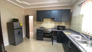 A kitchen with dark cabinets, a refrigerator, an oven, and a microwave. - 3-bedroom house at East Legon with 24hr security and solar powered lights (Accra)