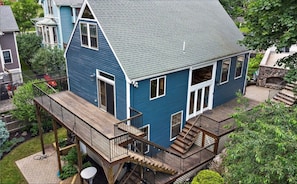 Ein zweistöckiges Haus mit blauer Fassade, einer Holzterrasse und einer Steintreppe, die zum Eingang führt.