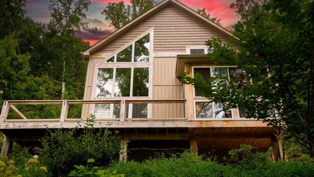 A wooden cabin with a deck, surrounded by dense forest.