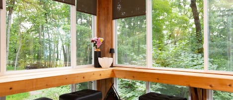 A corner seating area with a wooden bench and a table, large windows with a view of a forest.