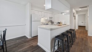 A modern kitchen with white cabinetry, a central island with stools, and a dark wood floor. - Fully Renovated & Private 2-bedroom home in Zephyrhills with Porch (Zephyrhills)
