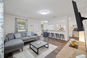 A modern living room with a grey sofa, a coffee table, and a kitchen area in the background. - Fully Renovated & Private 2-bedroom home in Zephyrhills with Porch (Zephyrhills)