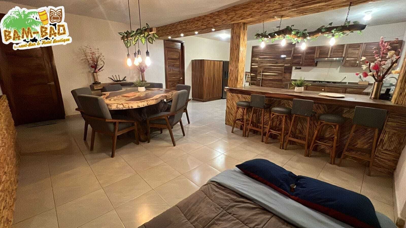 Una cocina amplia con comedor, una barra con taburetes y una cama con manta azul y roja.