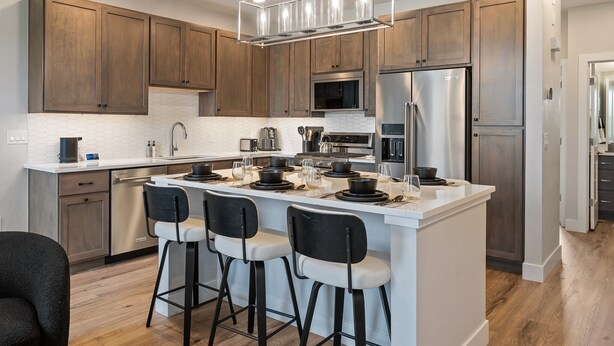 A modern kitchen with wooden cabinets, stainless steel appliances, a central island with bar stools, and a pendant light.
