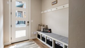 A hallway with a white door, a bench with storage drawers, and a coat rack with hooks.