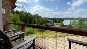 A balcony with wooden chairs and a stone wall, overlooking a grassy area with trees and buildings in the distance.