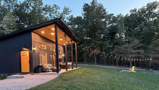 Une cabane moderne dotée d’un porche couvert, de meubles d’extérieur et d’une guirlande lumineuse.
