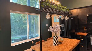 Une cuisine moderne avec une table à manger en bois, des meubles de rangement noirs et un luminaire suspendu.