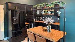 Une cuisine moderne avec des meubles de couleur noire, une table à manger en bois et un luminaire suspendu.