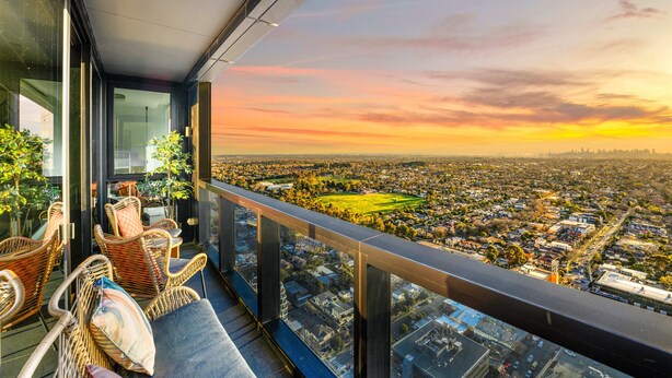 A balcony with wicker furniture overlooking a cityscape during sunset.