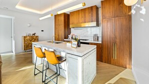 A modern kitchen with wooden cabinets, a marble island, and two bar stools.