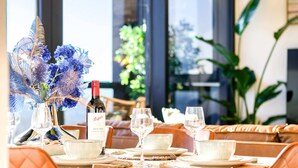 A dining area with a table set for four, featuring a bottle of wine, glasses, and a vase with blue flowers.