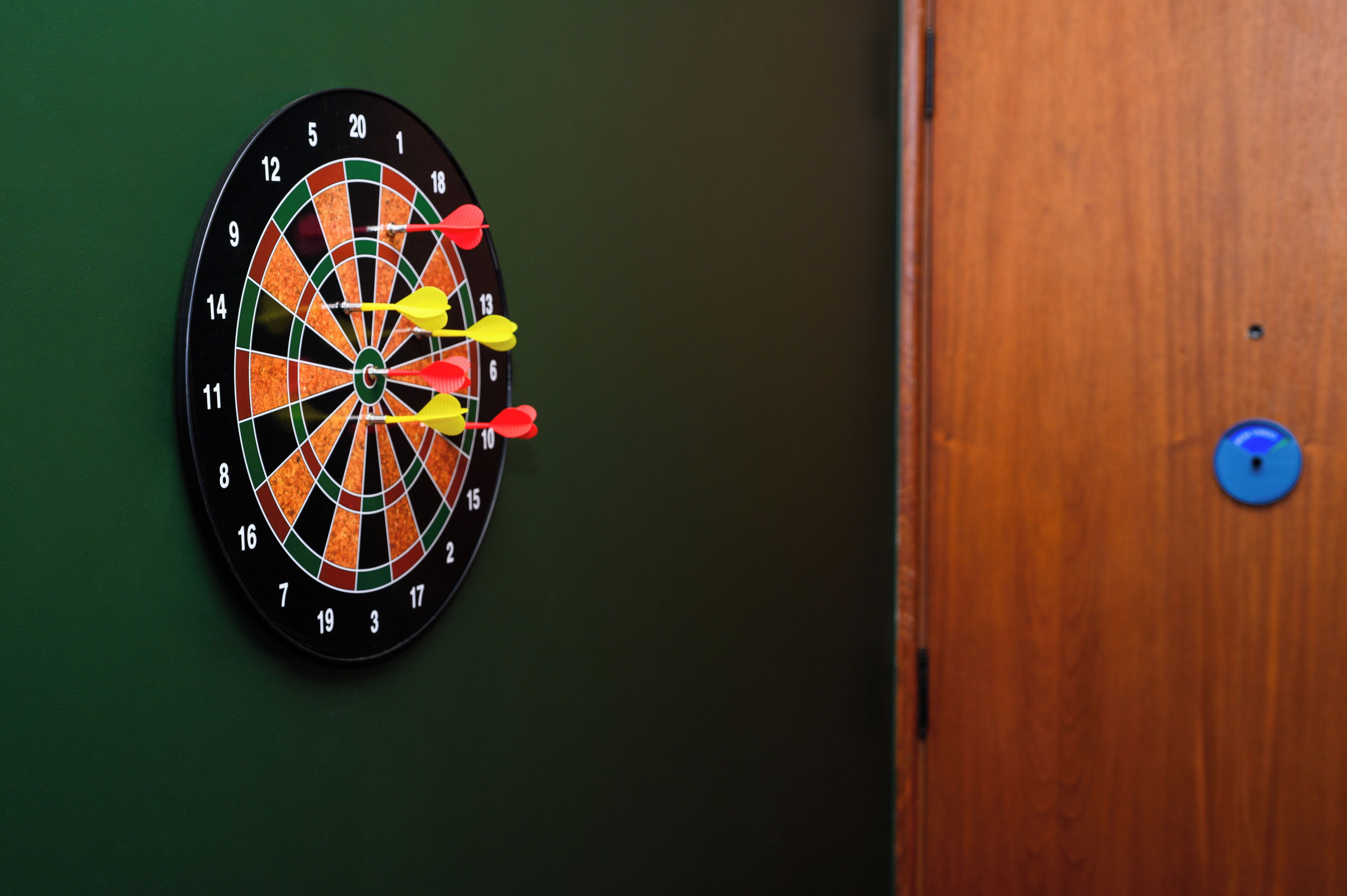 A dartboard with multiple darts on a green wall.