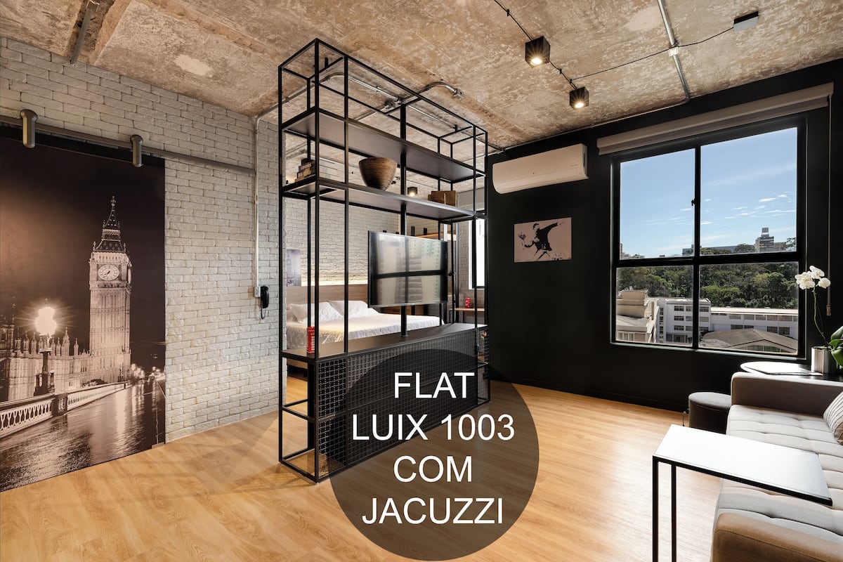 A modern room with a large window, a bed, a sofa, and a unique black shelving unit.