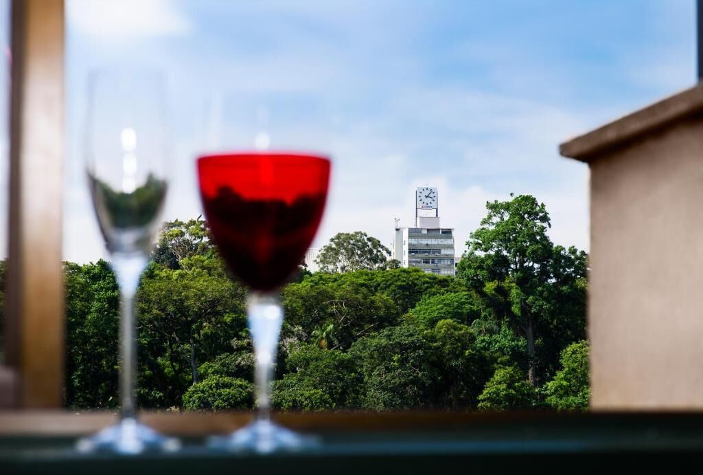 Two wine glasses on a table with a view of a clock tower and lush greenery in the background.