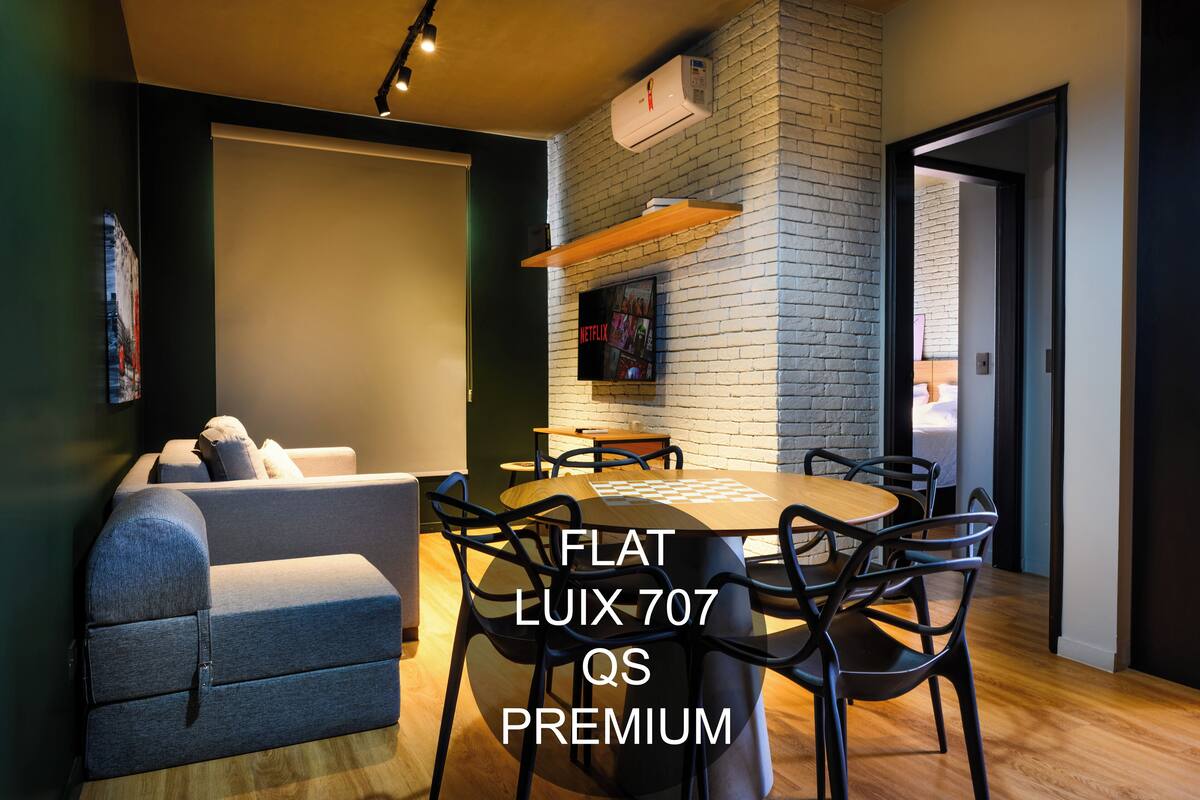 A modern living room with a flat-screen TV, a sofa, a dining table with chairs, and a brick wall.