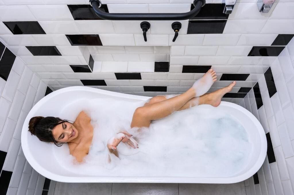 Una bañera llena de burbujas, un grifo negro y una pared de azulejos blancos con detalles en negro.