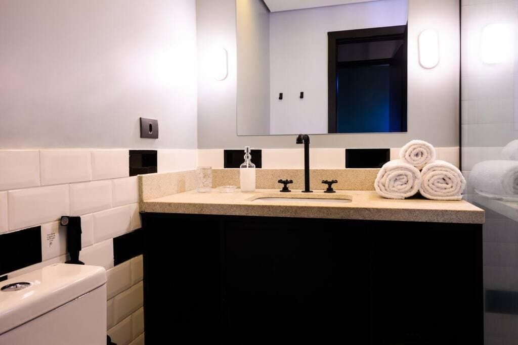 Een moderne badkamer met een beige aanrecht, een zwarte kraan en een spiegel boven de wastafel. Drie opgerolde handdoeken liggen op het aanrecht.