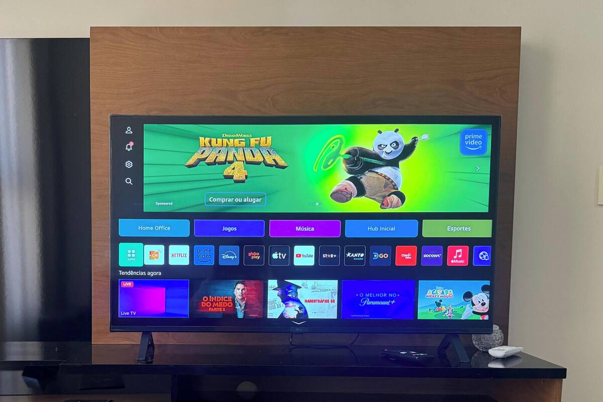 A flat-screen TV on a wooden TV stand with a remote control and a smartphone.
