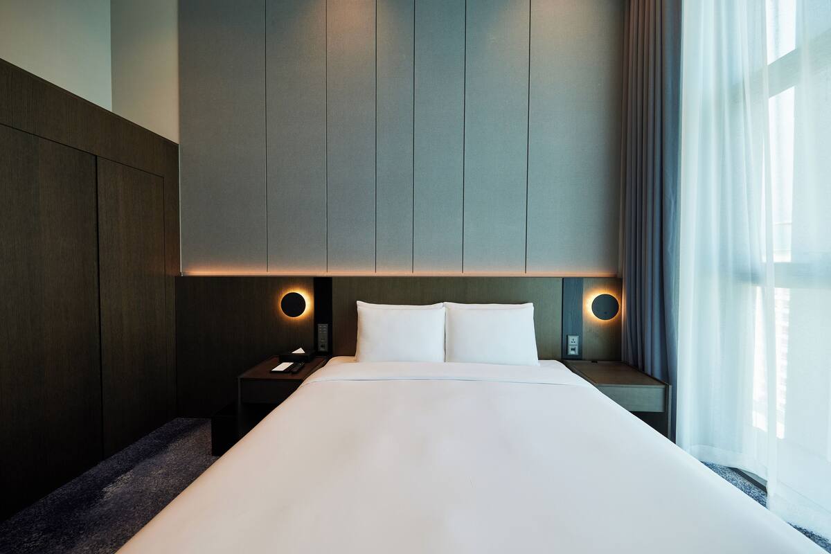 Habitació d'hotel moderna amb un llit gran, dues taules de nit i una petita taula auxiliar.