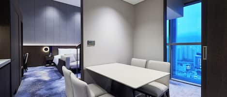A modern hotel room with a large window, a dining table, and a cozy seating area.