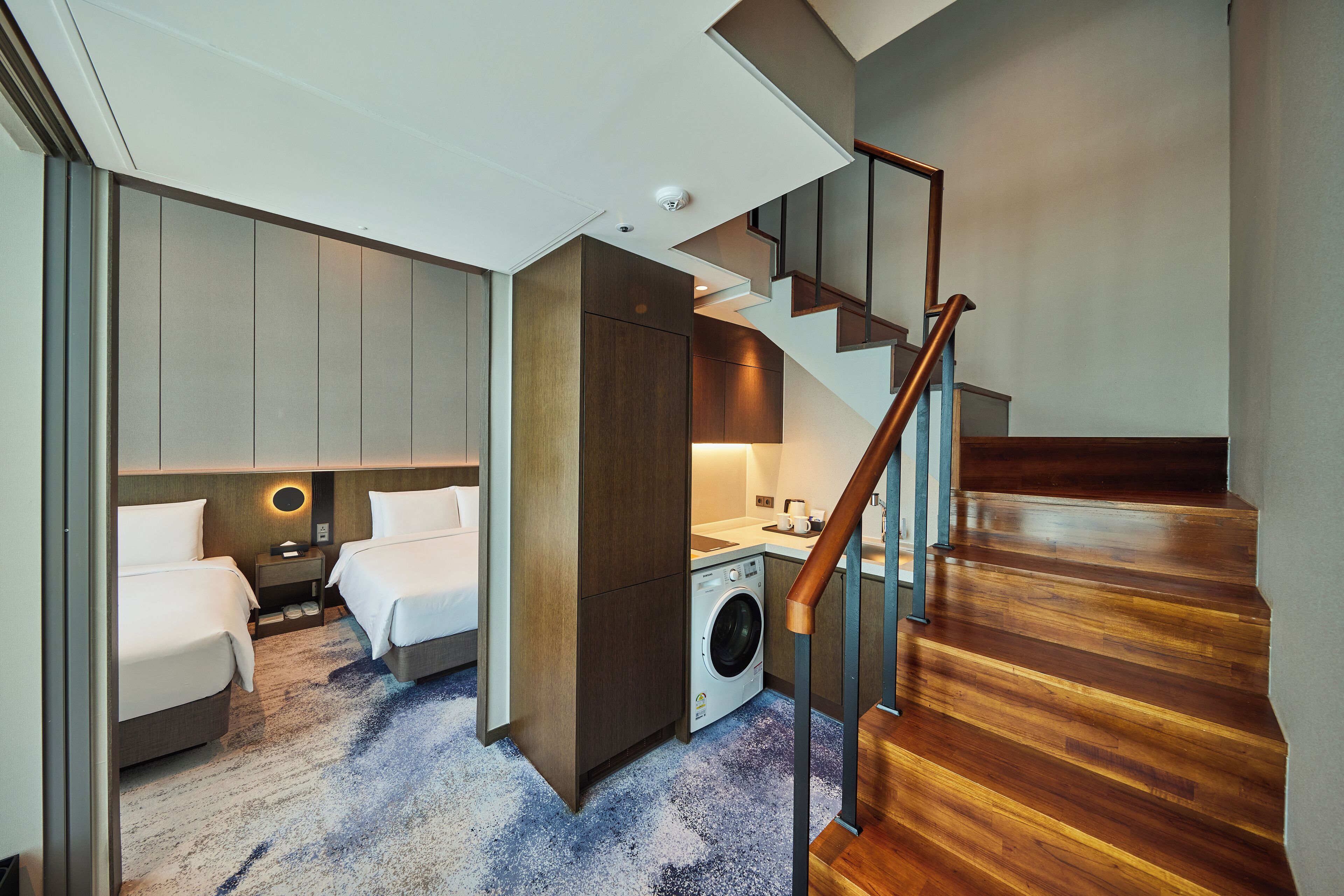 Habitación de hotel pequeña con cama, lavadora y una escalera.