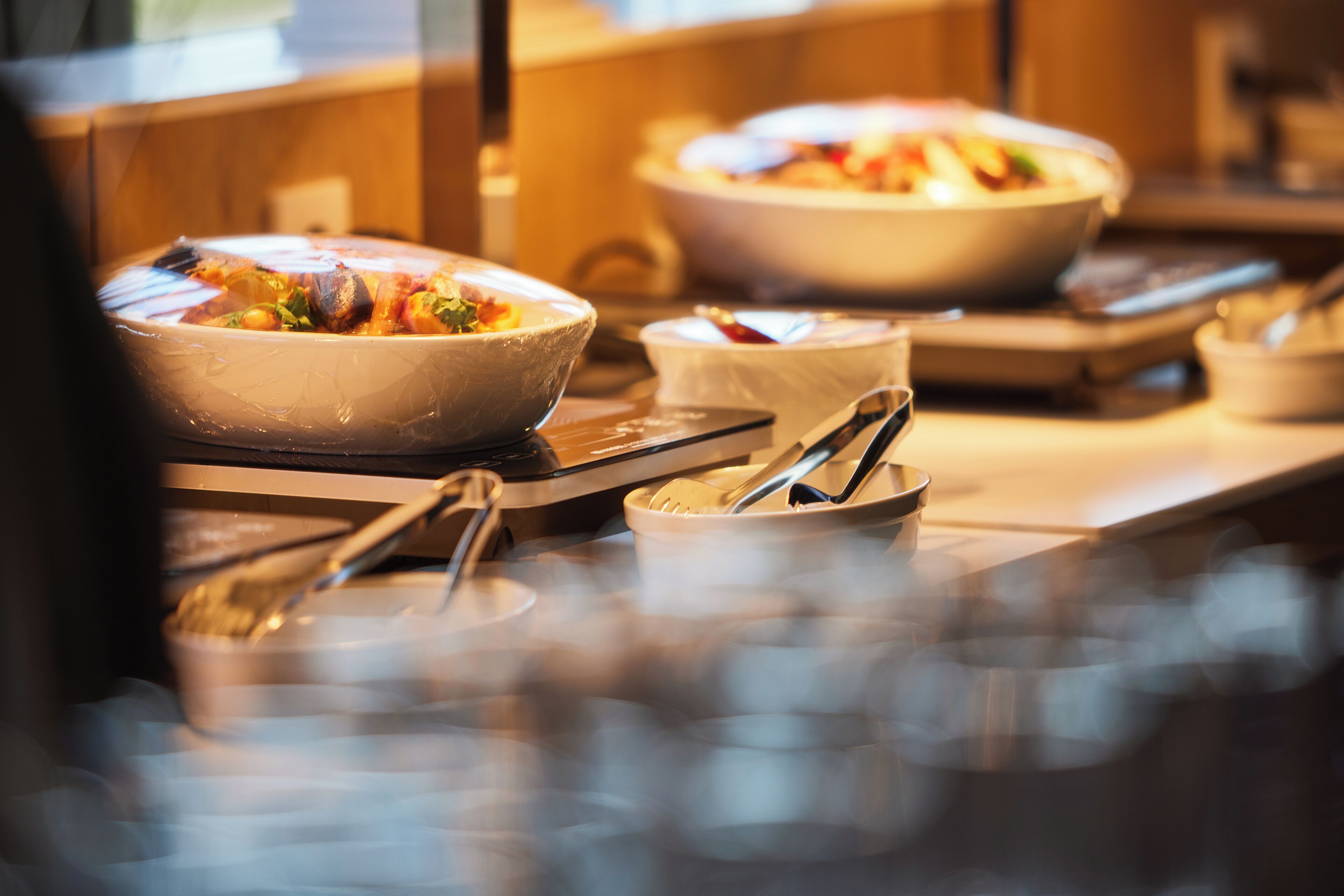 A buffet setup with multiple bowls of food, serving utensils, and a tiled floor.