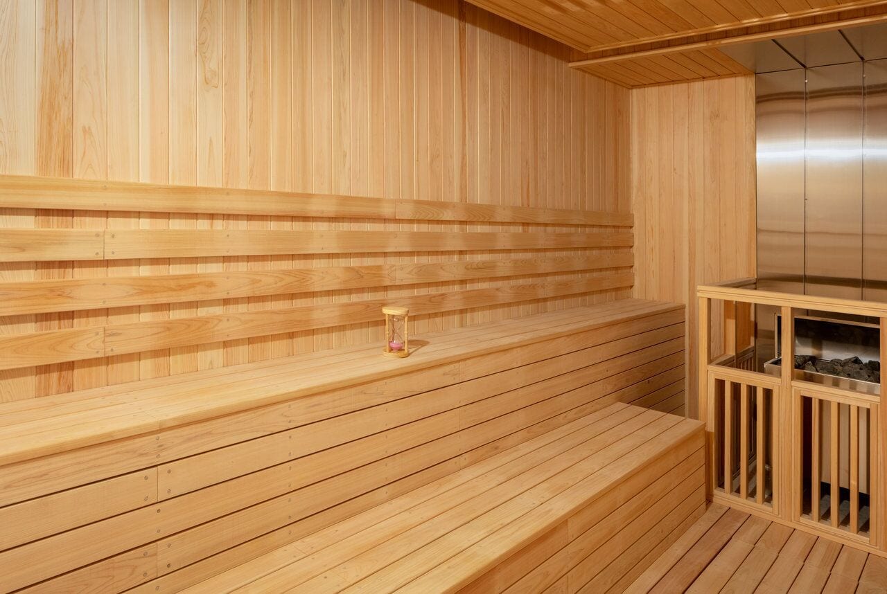 A wooden sauna with benches and a small hourglass on the floor.