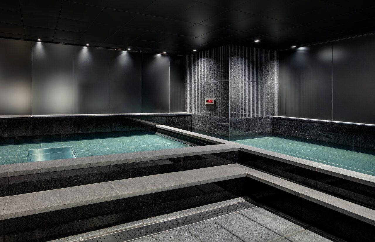 A modern indoor swimming pool with a minimalist design, featuring dark walls and a central water feature.