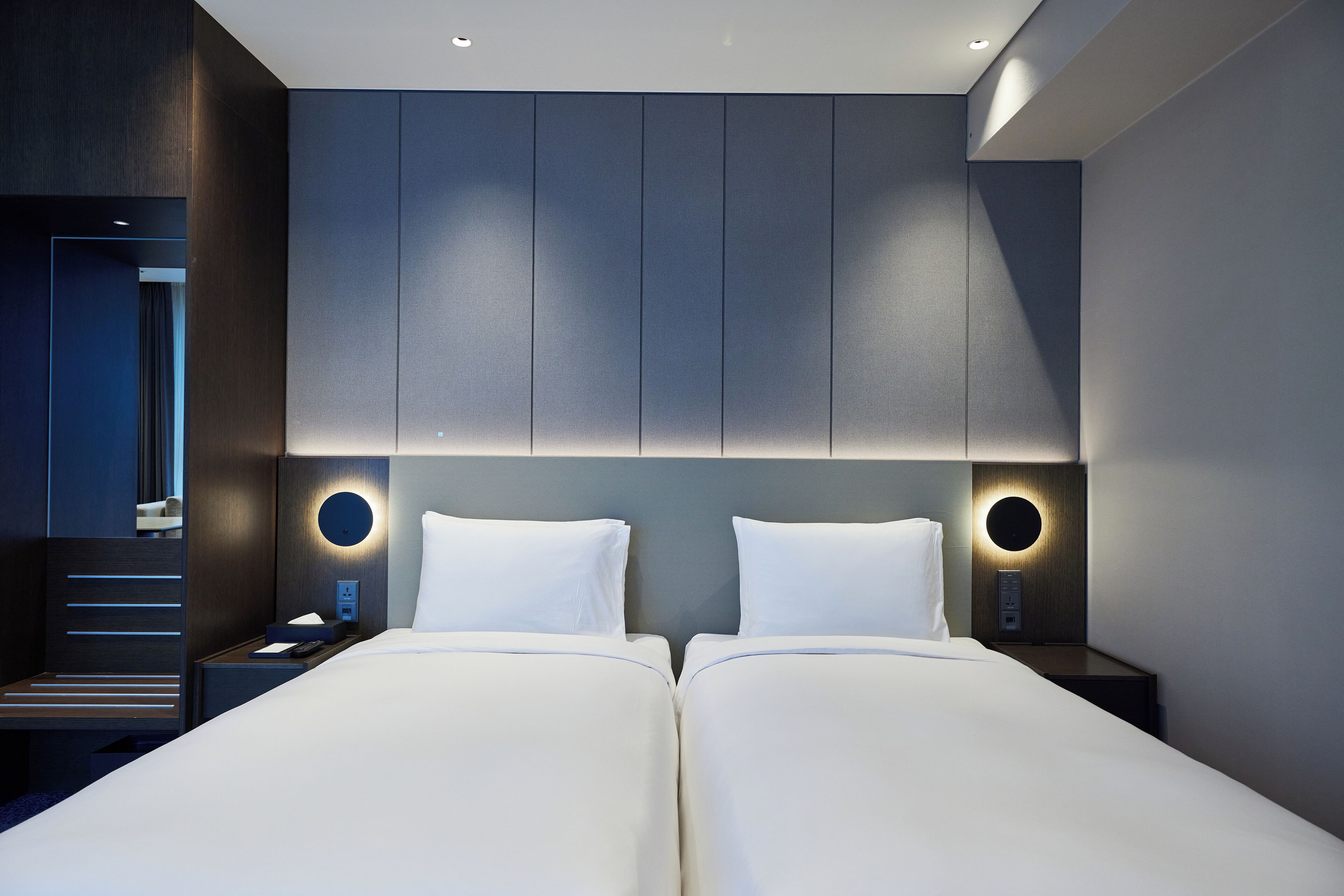 A modern hotel room with a large bed, bedside tables, and built-in lighting.