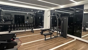 A modern gym with exercise equipment, large mirrors, and a wooden floor.