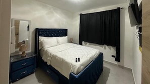 A bedroom with a bed, a nightstand, a mirror, and a TV.