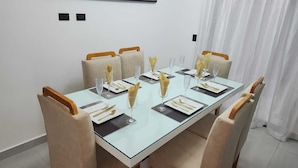 A dining table set for six with a glass top, beige upholstered chairs, and gold cutlery.
