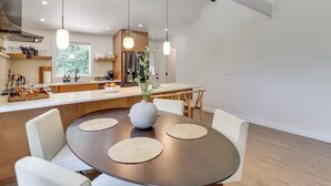 Eine moderne Küche mit Kochinsel, Pendelleuchten und einem Essbereich mit rundem Tisch und Stühlen.