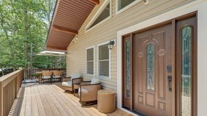 Eine Holzterrasse mit Gartenmöbeln, eine überdachte Veranda und eine große Haustür mit dekorativen Glasscheiben.
